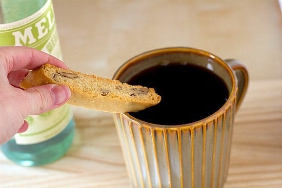 Hand holding a piece of anisette biscotti over a cup of coffee.