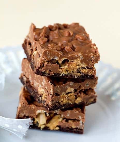 Stack of 3 peanut butter cup crunch brownie bars on a white plate.