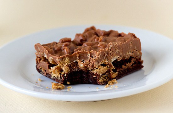 One peanut butter cup crunch brownie bar with a bite taken from it on a white plate.
