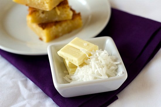 White chocolate squares and shredded coconut in a square white bowl.