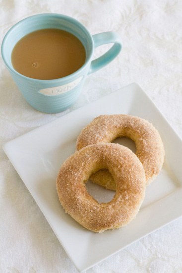2 cinnamon sugar doughnuts on a white square plate with a cup of coffee.