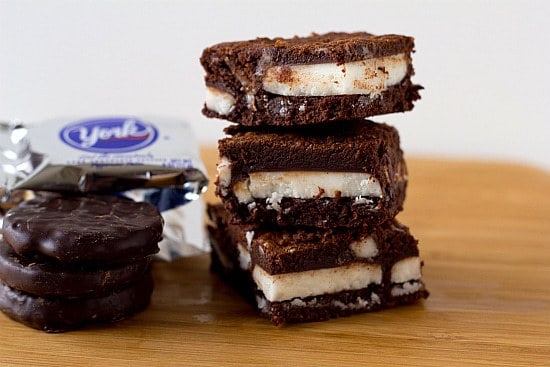 Stack of 3 chocolate mint brownies next to a stack of York peppermint patties on a wood surface