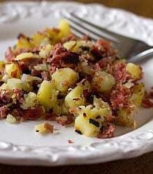Serving of corned beef hash on a white plate with a fork.