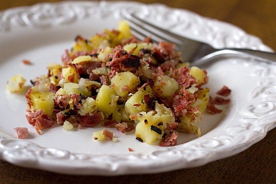 Serving of corned beef hash on a white plate with a fork.