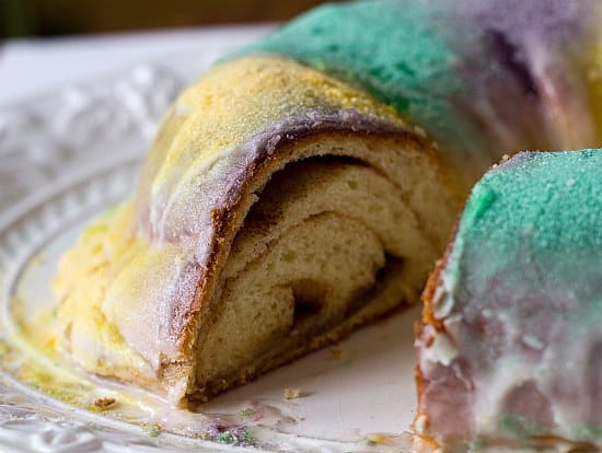 Mardis Gras king cake with a slice removed showing the swirled inside.