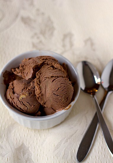 Scoops of chocolate peanut butter cup ice cream in a white bowl with 2 spoons next to the bowl.