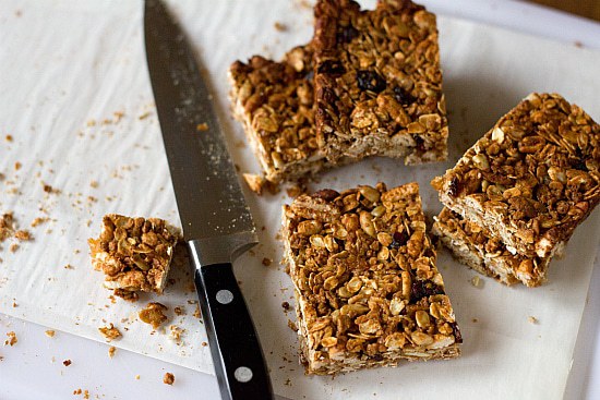 Homemade granola bars cut into squares on a parchment paper lined cutting board with a knife.