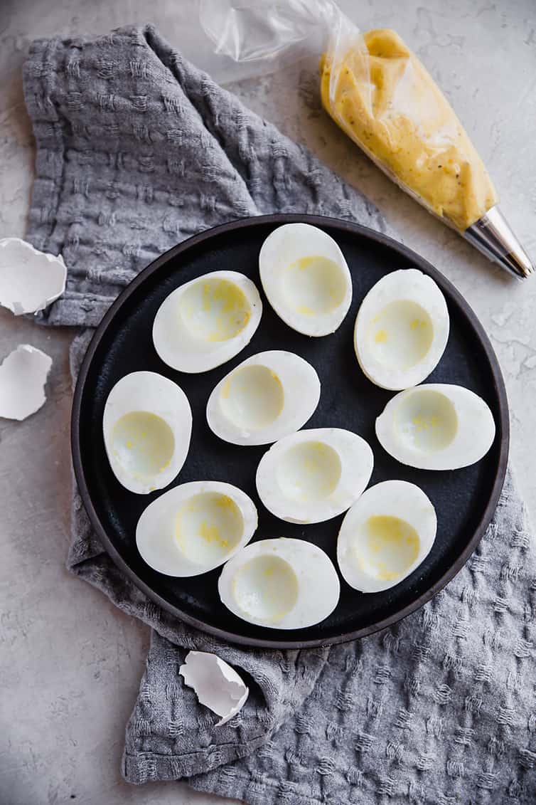 A platter with egg white halves next to a piping bag of filling.