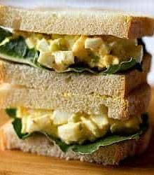 Stack of 2 egg salad sandwiches on a wood board.