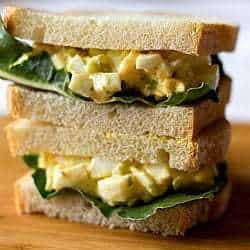 Stack of 2 egg salad sandwiches on a wood board.