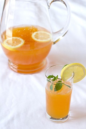Ginger tea lemonade in a glass garnished with a lemon round and a glass pitcher of ginger tea lemonade.