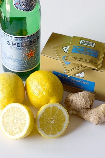 Ingredients for ginger tea lemonade including sparkling water, lemons, fresh ginger, and tea bags.