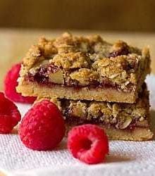 Stack of 2 raspberry streusel bars on a paper towel on a wood surface.