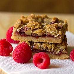 Stack of 2 raspberry streusel bars on a paper towel on a wood surface.