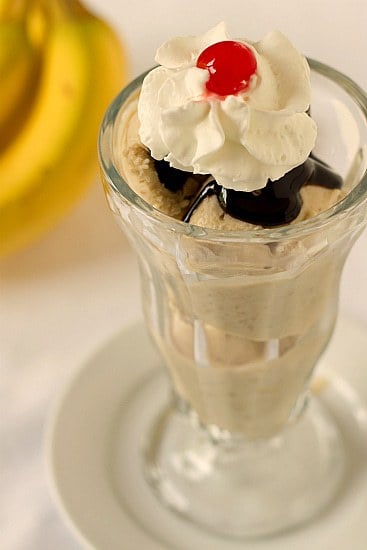 Scoops of roasted banana ice cream in a glass topped with hot fudge, whipped cream, and a cherry.