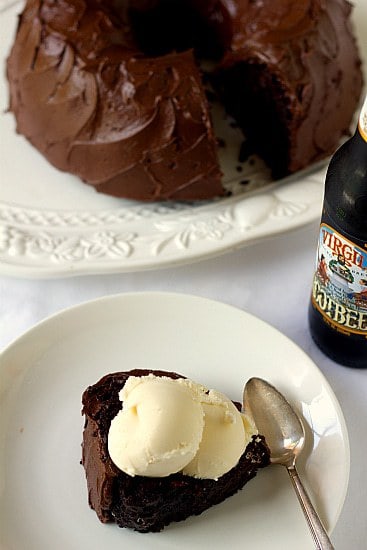Overhead image of a slice of root beer float cake topped with vanilla ice cream on a white plate with a spoon and the frosted cake in the background.