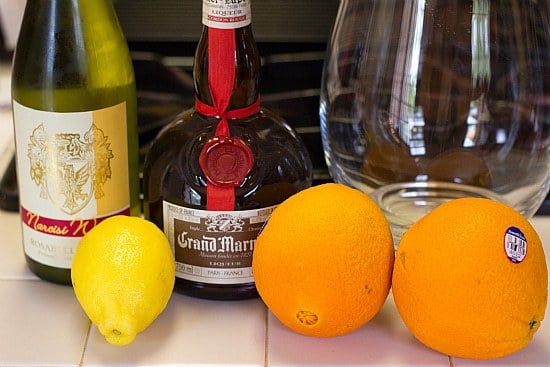 Ingredients for white sangria including wine, liquor, oranges, and a lemon.