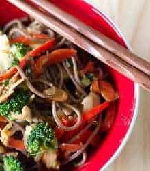 Soba noodle stir fry in a red bowl with chopsticks.