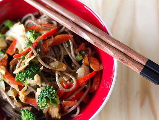 Overhead image of a serving of soba noodle stir fry with chopsticks in a red bowl.