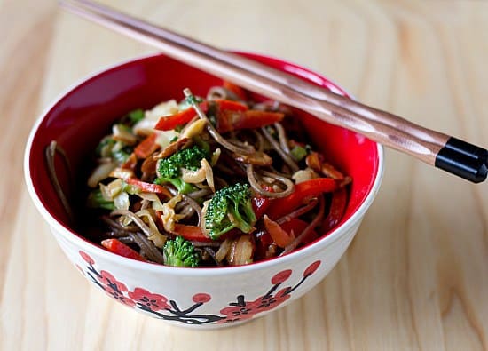 A serving of soba noodle stir fry with chopsticks in a red bowl.
