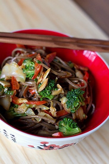 A serving of soba noodle stir fry with chopsticks in a red bowl.