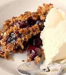 A serving of cherry crisp with vanilla ice cream in a white bowl with a spoon.