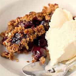 A serving of cherry crisp with vanilla ice cream in a white bowl with a spoon.