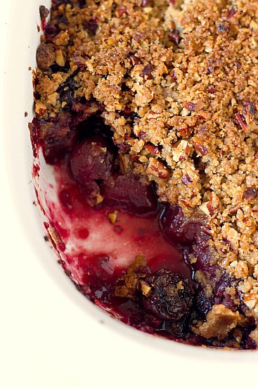 Overhead image of cherry crisp with a few scoops removed in a white baking dish.