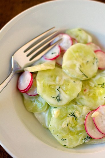 Overhead image of creamy cucumber salad in a white bowl with a fork.