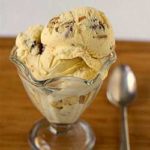 Scoops of date, rum, and pecan ice cream in a glass bowl with a spoon.
