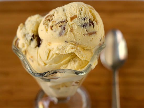 Scoops of date, rum, and pecan ice cream in a glass bowl with a spoon.
