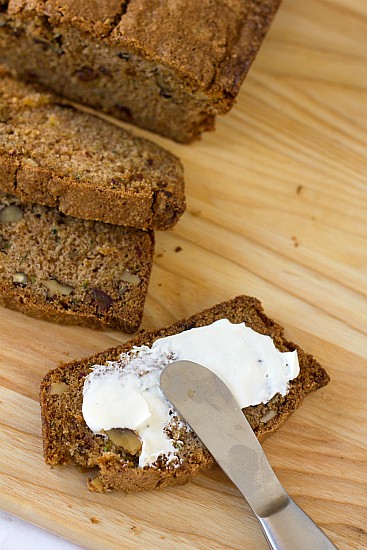 Overhead image of slices of zucchini pineapple bread on a wood cutting board with butter spread on a slice with a knife.