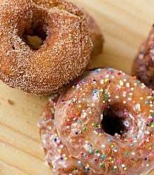 Overhead image of cinnamon sugar buttermilk doughnuts and glazed buttermilk doughnuts with nonpareil sprinkles on a wood surface.