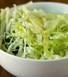 Sliced cabbage with oil and vinegar in a white bowl.