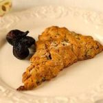 A honey fig scone on a white plate with dried figs as garnish.