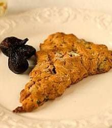 A honey fig scone on a white plate with dried figs as garnish.