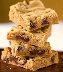 Stack of 4 peanut butter chocolate chip cookie bars on a wood surface.