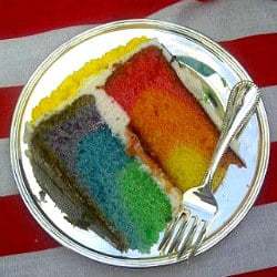 Slice of layered rainbow cake on a plate with a fork.