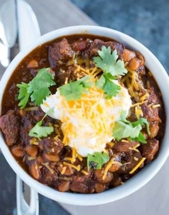 A bowl of chili con carne topped with sour cream, shredded cheese and cilantro.