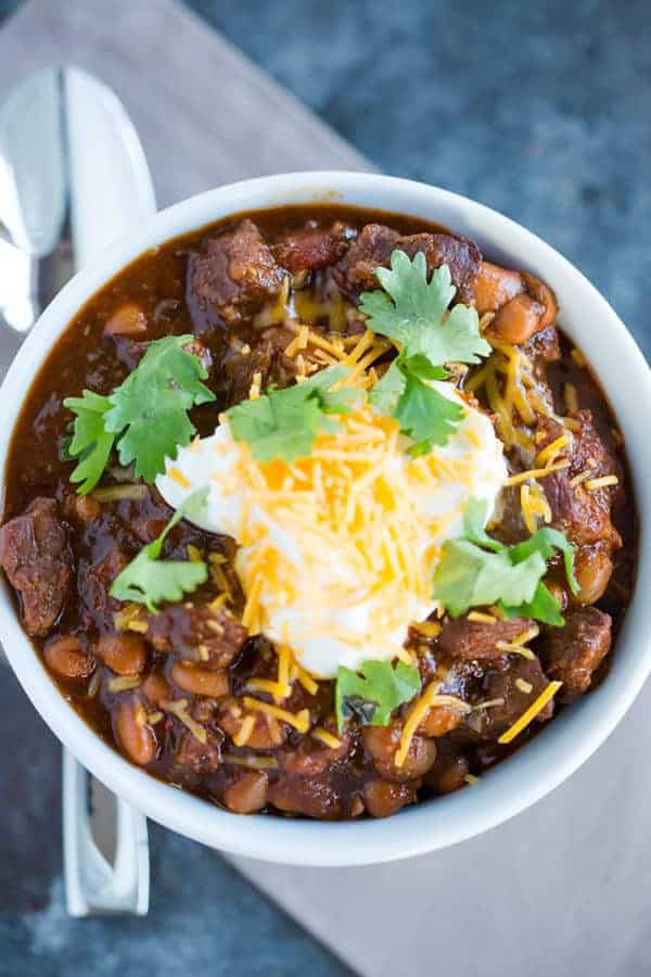 A bowl of chili con carne topped with sour cream, shredded cheese and cilantro.