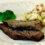 Serving of roast lamb on a white plate with potatoes and vegetables.