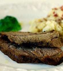 Serving of roast lamb on a white plate with potatoes and vegetables.