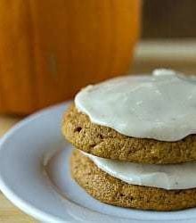 Stack of 2 pumpkin cookies topped with brown butter icing on a white plate.