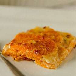 Serving of sweet potato gratin on a white plate with a fork.