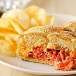 Chipotle ham BBQ sandwich cut in half with potato chips on a white plate.