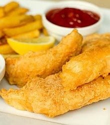 Beer battered cod and french fries on a white plate with lemon wedges, tartar sauce in a white bowl, and ketchup in a white bowl.