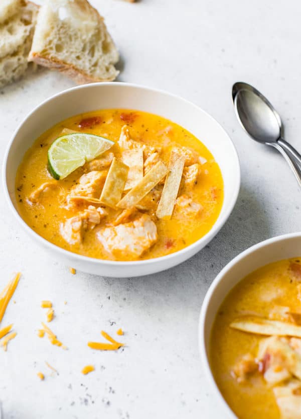 A bowl of chicken tortilla soup with bread and spoons in the background.