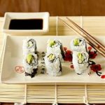 Sushi rolls on a white plate with chopsticks.