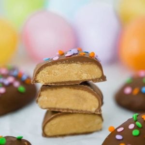 Peanut butter eggs, cut in half and stacked with Easter eggs in the background.