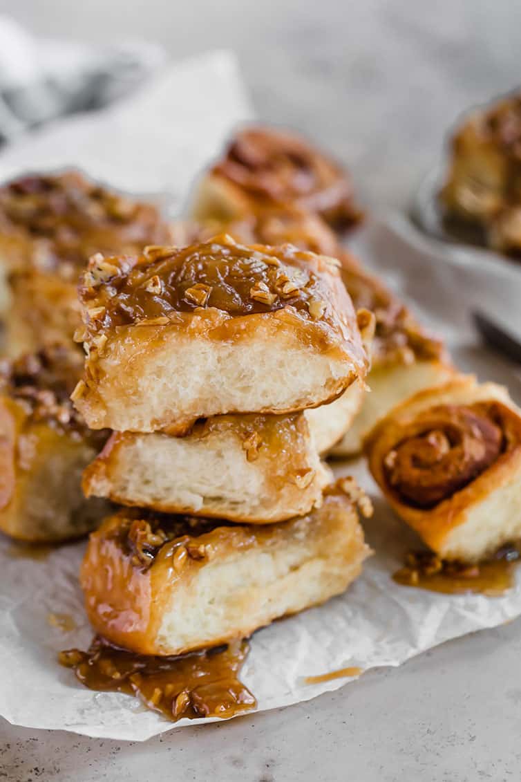 A stack of three sticky buns on parchment paper, with others in the background.